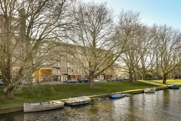 Woongebouw aan de Cornelis Dopperkade met bomen en afgemeerde bootjes langs het water.
